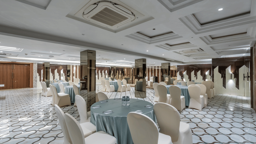 A conference hall with round tables draped in blue cloths and white chairs on a geometric tiled floor | Lawrence Solitaire Resort, Nainital
