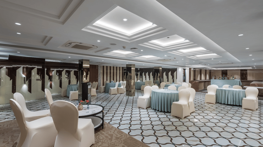 A large banquet hall with white chairs arranged around circular tables on a white and grey patterned floor | Lawrence Solitaire Resort, Nainital