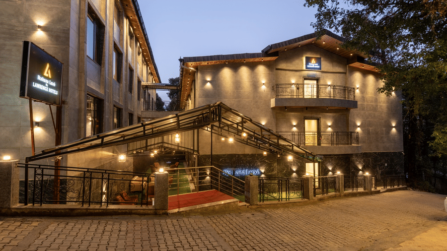 An evening exterior view of a multi-storey building with lit windows and a glass-roofed entrance area | Lawrence Solitaire Resort, Nainital