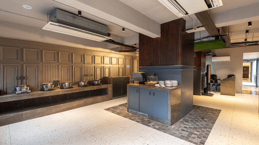 A buffet area with food warmers along a grey wall and a central service station on a patterned tile floor | Lawrence Solitaire Resort, Nainital