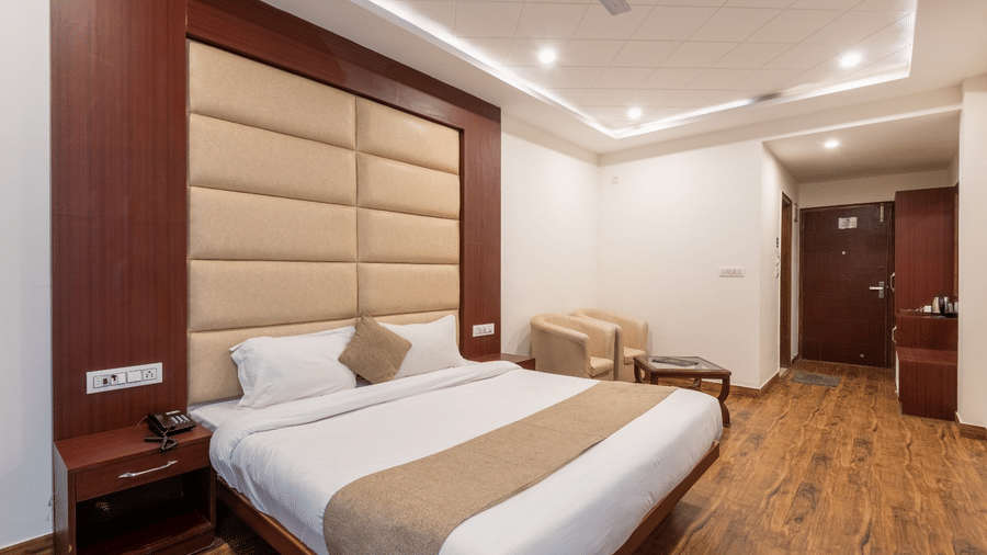 A hotel room at Shining Hills, Mussoorie with a large bed, wooden flooring, ceiling fan, and padded wall panels.
