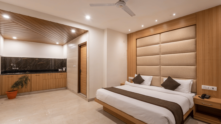 A hotel room at Shining Hills, Mussoorie with a double bed, ceiling fan, side table, and padded wall panels.