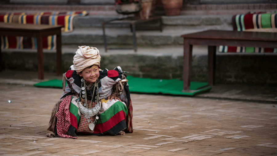 An elderly Newari woman in traditional clothing resting in a historic brick courtyard square in Bhaktapur, Nepal.