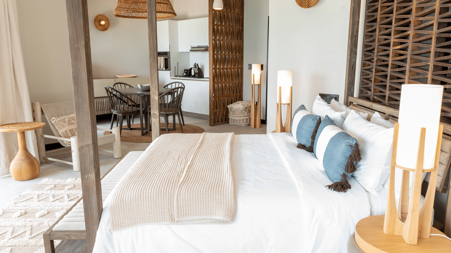 A studio room with a plush bed, natural wood accents, and a seamless flow into a dining area at the Tamarind Hills Resort and Villas, Antigua.