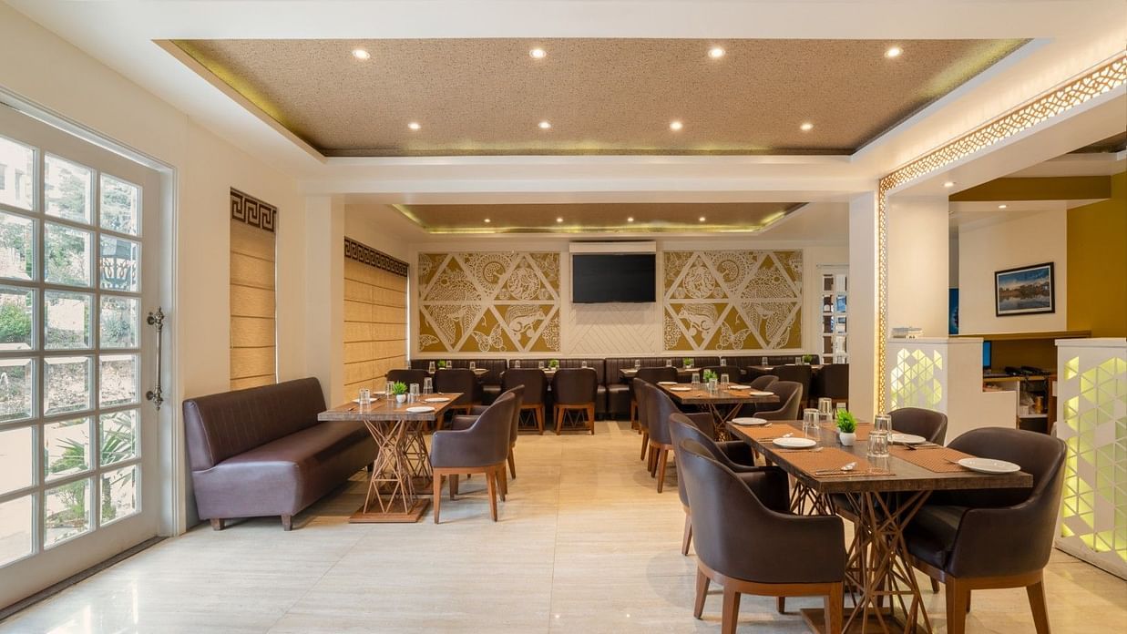 The Bridge restaurant at Clarks Inn, Near Kainchi Dham offers modern seating, set tables, and decorative wall panels with recessed ceiling lights.