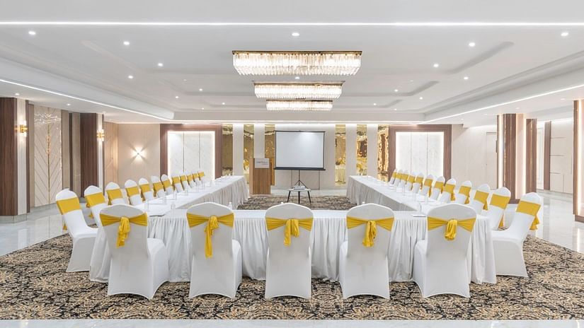 A conference room with white-covered chairs tied with yellow bows, a long U-shaped table, and a projector screen at the front – Clarks Inn Suites, Near Taj Mahal.