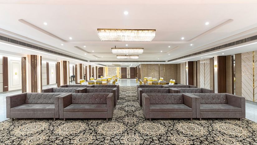 A spacious banquet hall with elegant patterned carpets, plush brown sofas, and chandeliers hanging from the ceiling – Clarks Inn Suites, Near Taj Mahal.