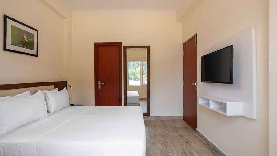 Room features a double bed with white linens, a wall-mounted television, two wooden doors, a full-length mirror, and a framed picture at Clarks Inn, Near Kainchi Dham.