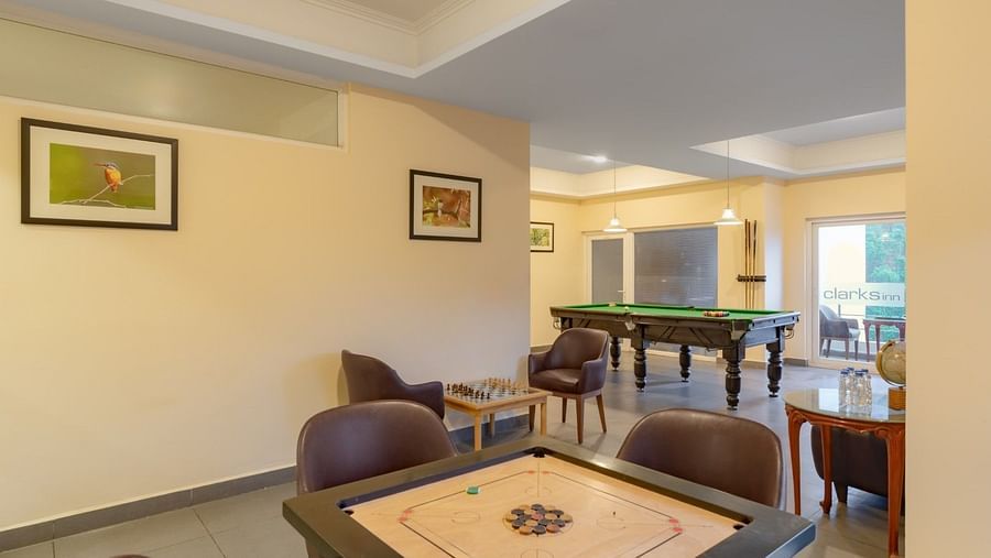 Game room at Clarks Inn, Near Kainchi Dham features a carrom board, a pool table, a chess set, comfortable seating, and framed pictures on the walls.