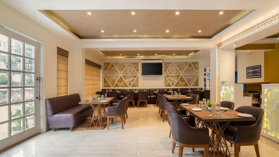 The Bridge restaurant at Clarks Inn, Near Kainchi Dham offers modern seating, set tables, and decorative wall panels with recessed ceiling lights.