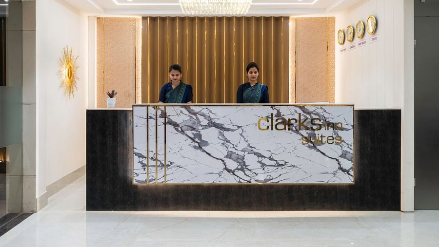 The Clarks Inn Suites reception desk with two female staff in blue uniforms and the hotel's logo on the front panel. – Clarks Inn Suites, Near Taj Mahal