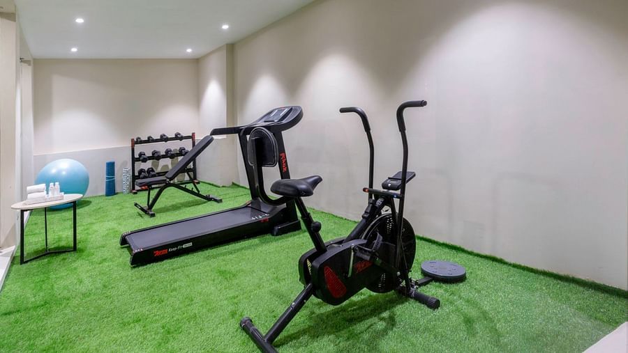 A compact fitness centre with a treadmill, elliptical, stationary bike, dumbbells, and artificial turf flooring. – Clarks Inn Suites, Near Taj Mahal