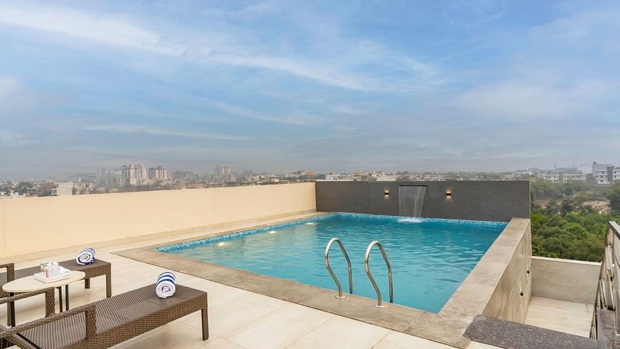 A rooftop swimming pool with a city view, surrounded by a beige deck with sun loungers. – Clarks Inn Suites, Near Taj Mahal