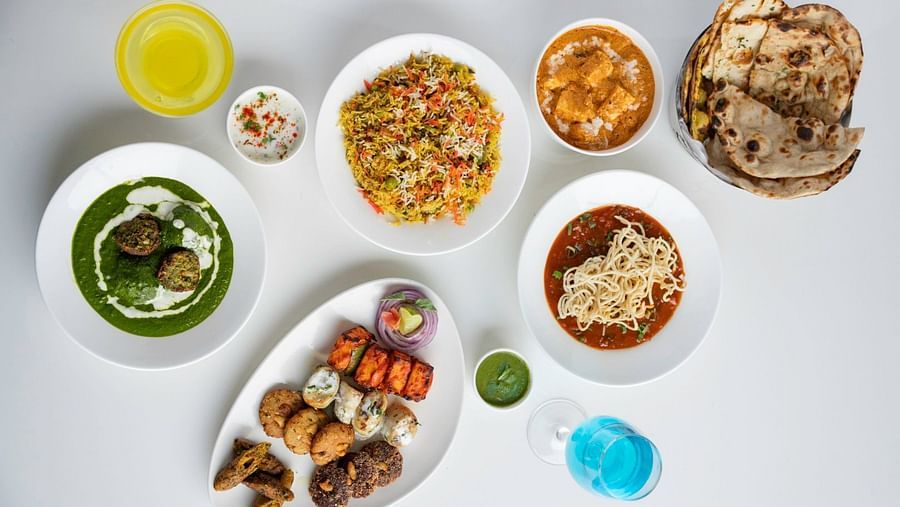 A variety of Indian and continental dishes, including biryani, butter chicken, naan, pasta, and appetisers, served on a white table. – Clarks Inn Suites, Near Taj Mahal