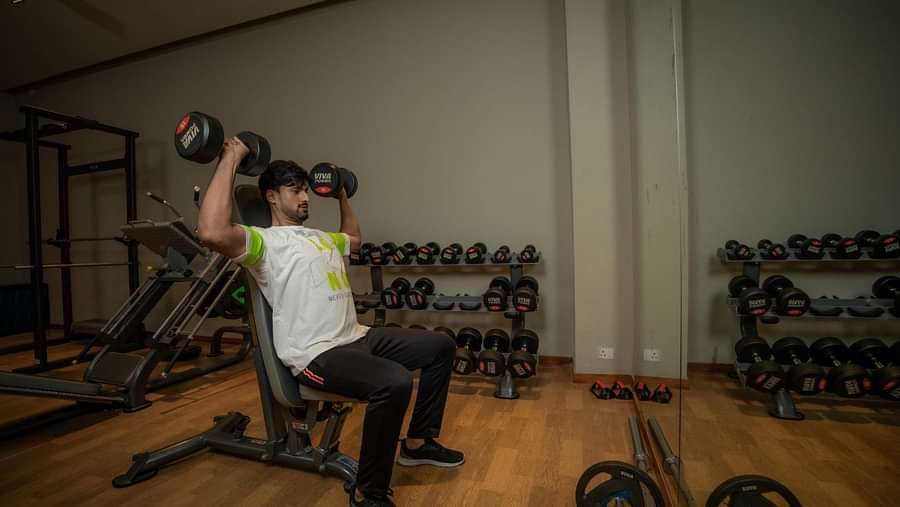 A person performing the shoulder press with dumbbells at the indoor gym at Singalila Club