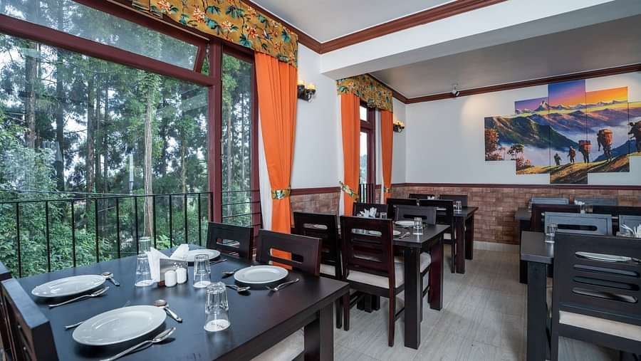 Image of a dining space with large windows and seating area at Summit Sherpa Mountain Hotel & Spa, Kalimpong