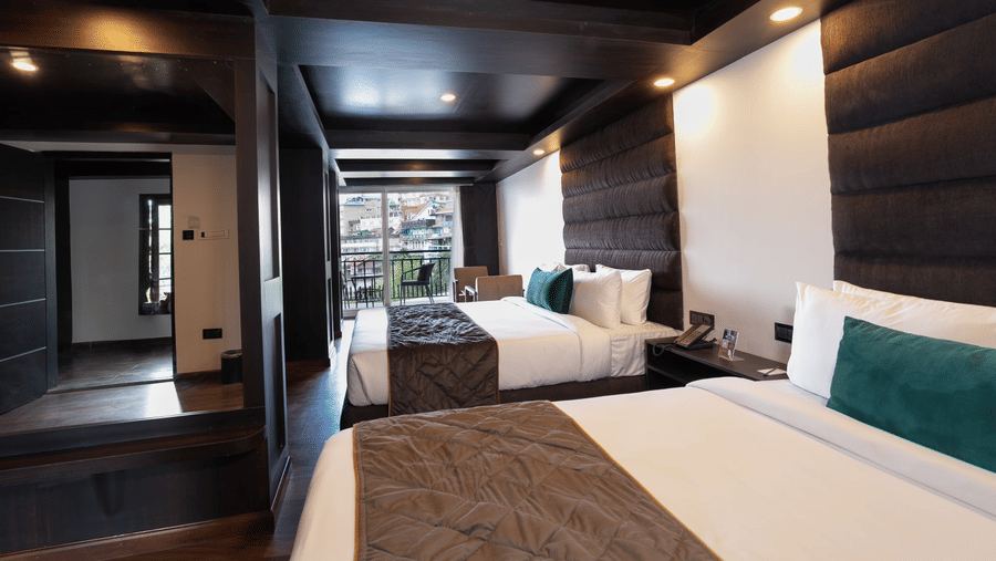 Guest room at The West Gate Posada By Summit, Darjeeling, featuring two beds arranged in separate sections with wooden panelling.