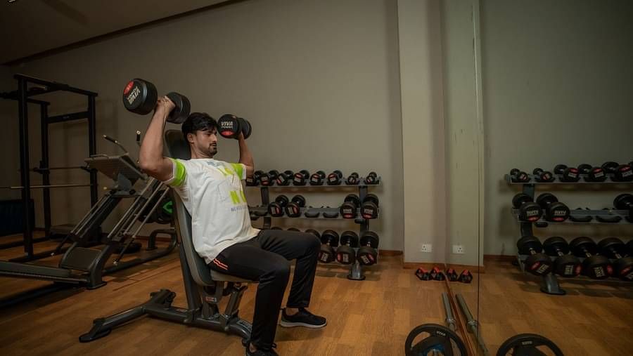 A person performing the shoulder press with dumbbells at the indoor gym at Singalila Club