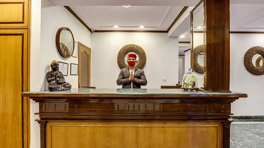 The staff at the reception desk stands behind the wide wooden counter, warmly welcoming guests at Summit Le Royale Hotel, Shimla