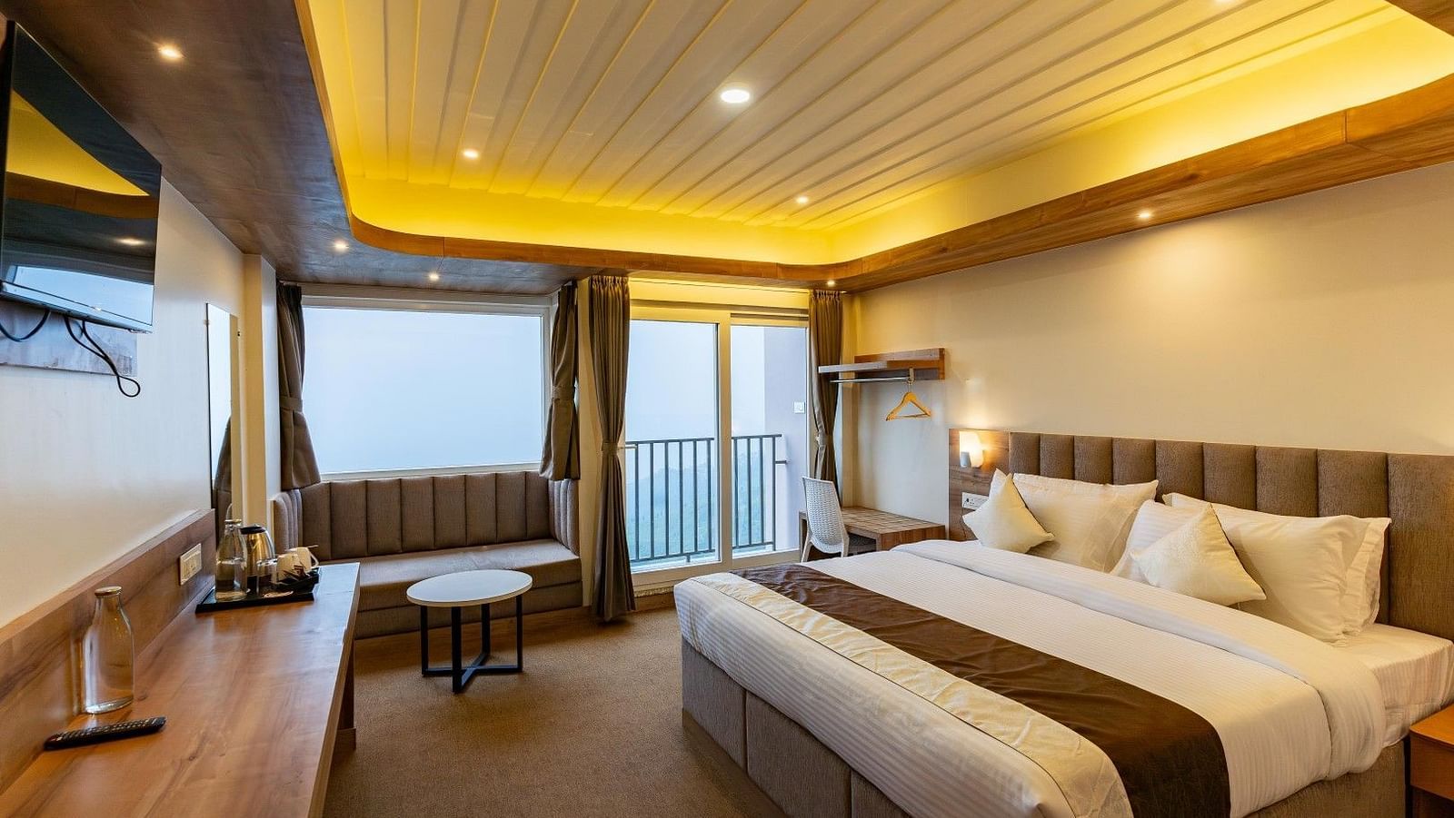 An image of a bedroom with ceiling lights, flat TV screen, a seating area and a balcony - Avianna Group of Hotels & Resorts