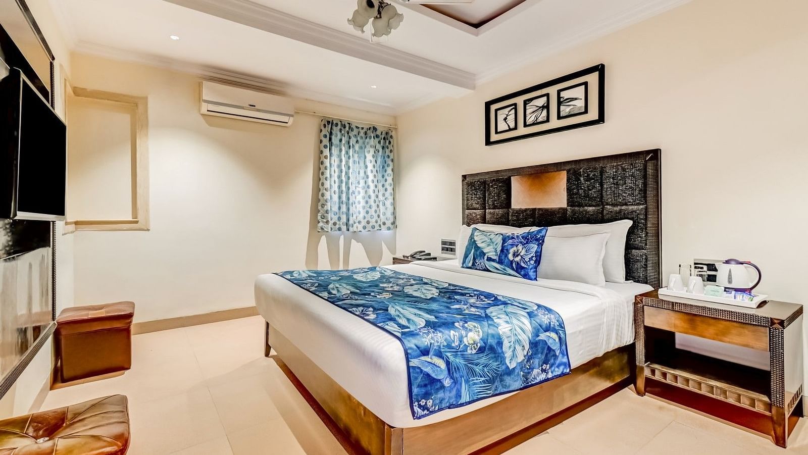 Spacious bed accompanied by a wooden side table, a wall-mounted television, and a wooden console positioned beneath it