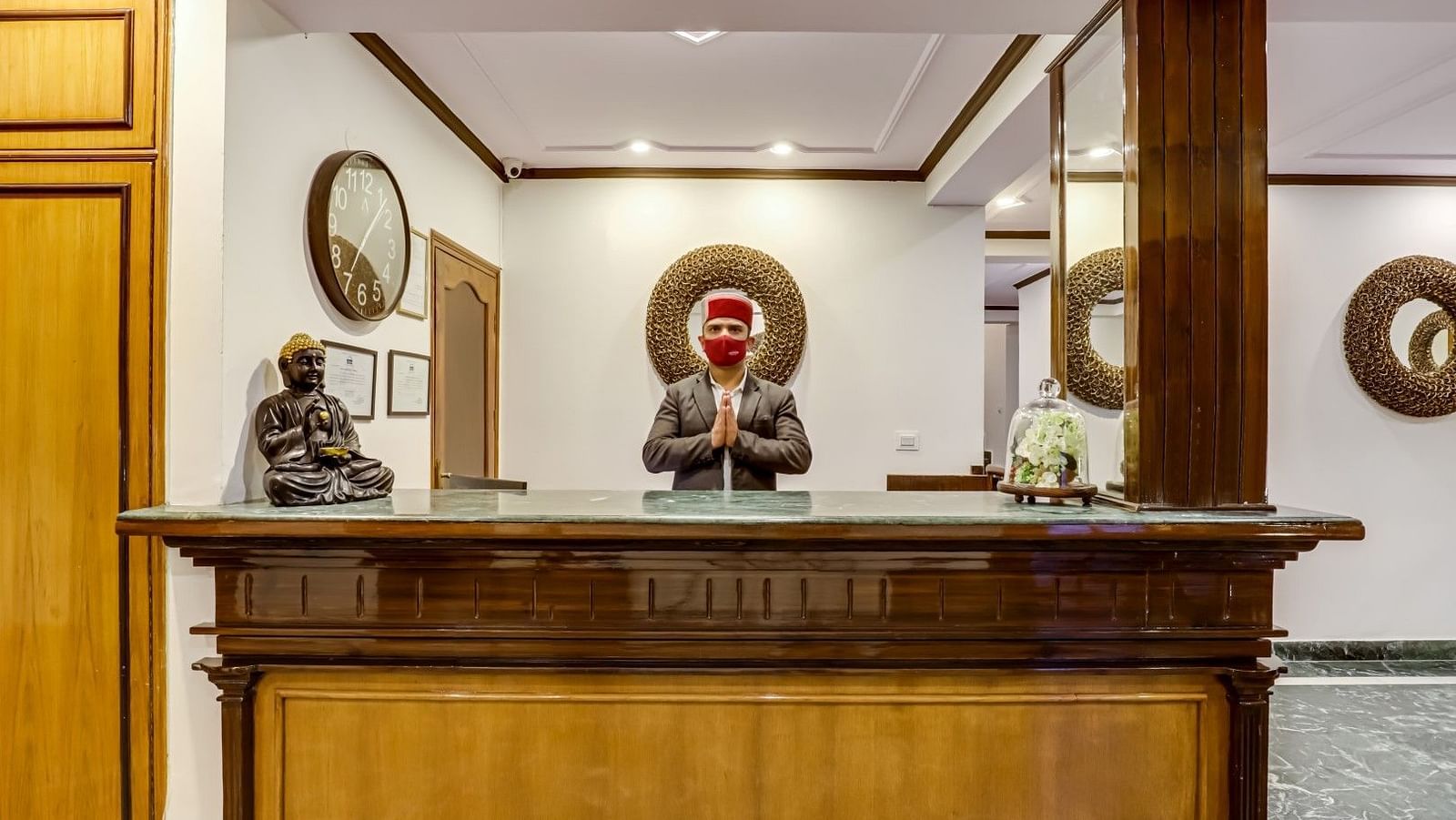 The staff at the reception desk stands behind the wide wooden counter, warmly welcoming guests at Summit Le Royale Hotel, Shimla