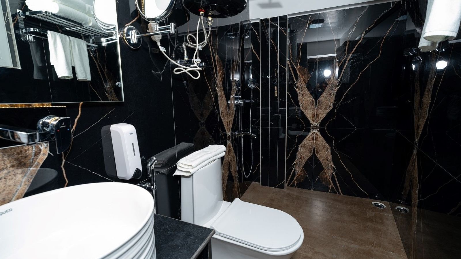 Image of a washroom with black tiles, a white basin and towels hanging along with other amenities.