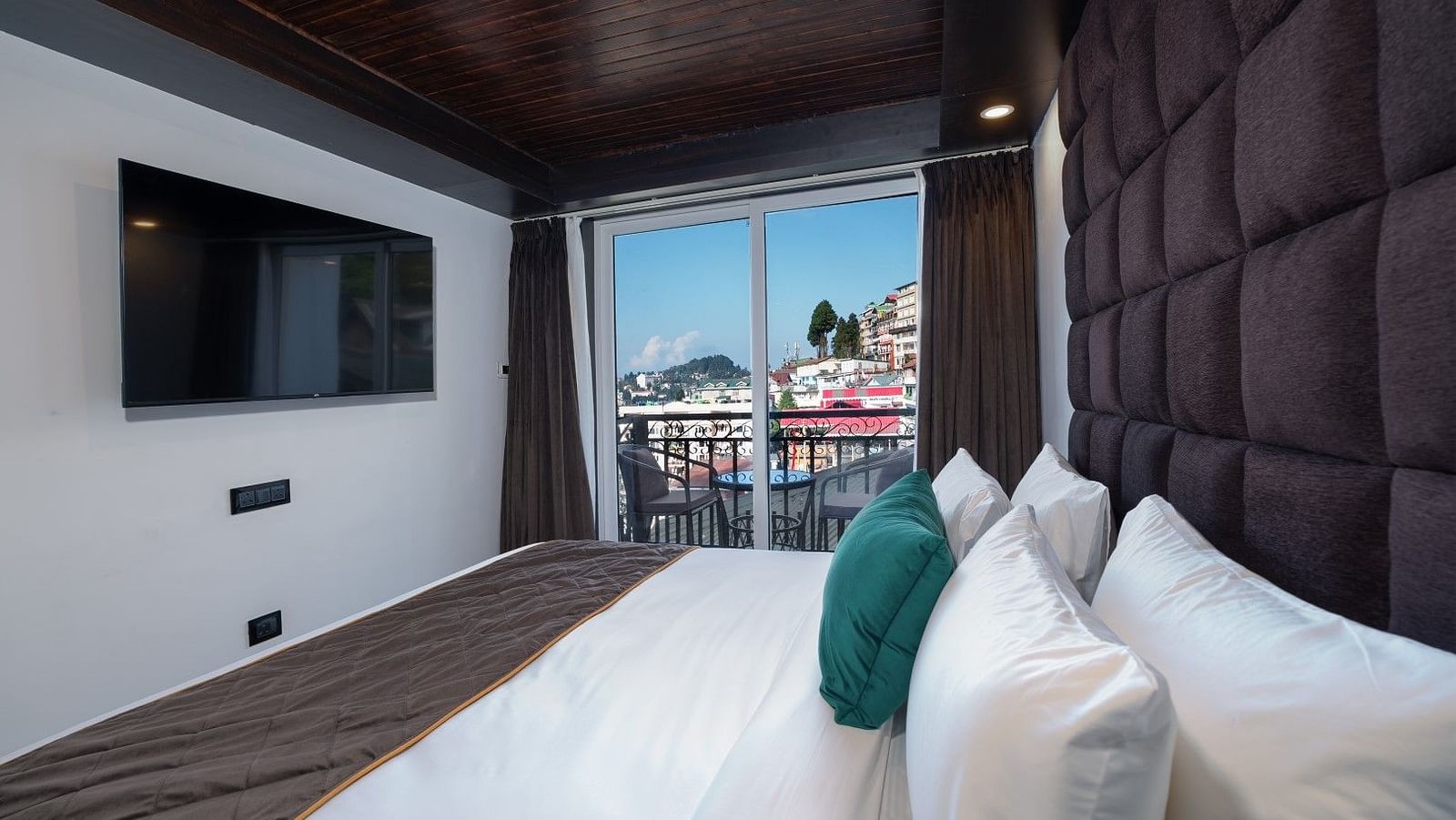 A side-angle view of the room highlighting the bed and LED TV, with a glimpse of the private balcony.