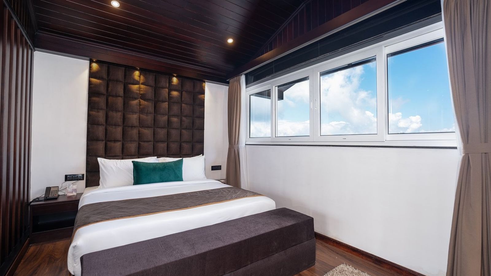 Image of a bed in a well furnished room along with an expansive window. 