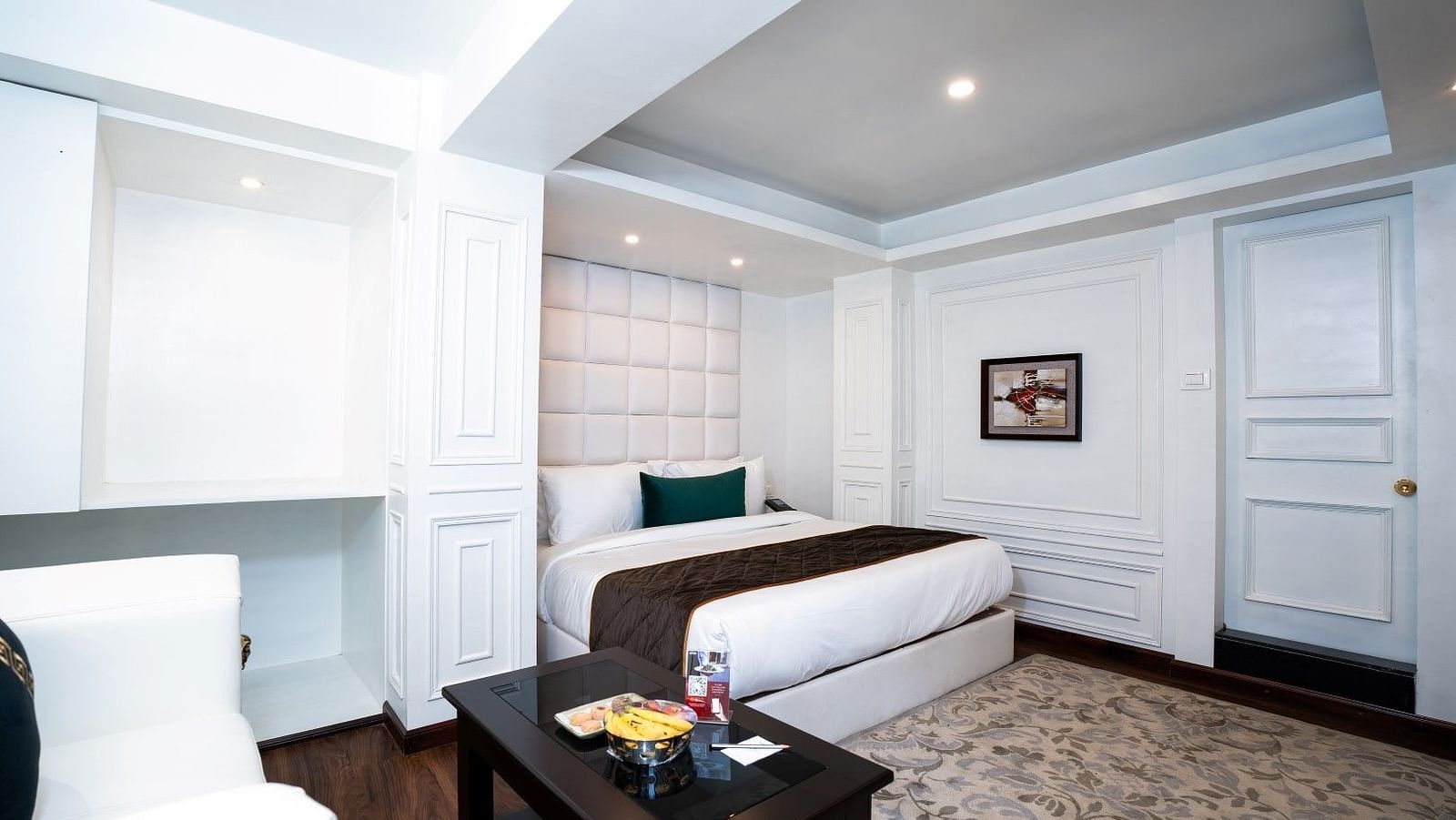 A shot of the room from different angel featuring a king-size bed with crisp white linens, ambient lighting, and a sofa with a side table.