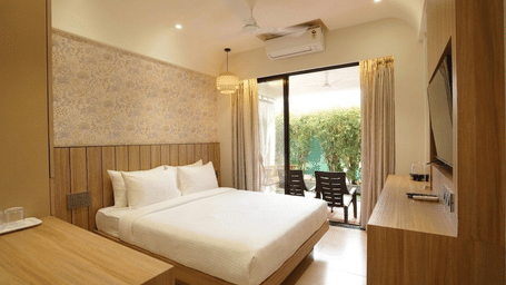 A queen size bed, a wooden television console, and glass balcony doors at Bougainvillea, Alibaug.