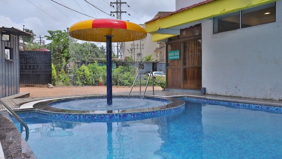 Outdoor swimming pool area with a separate circular kids’ pool featuring a mushroom-shaped water feature, pool ladders, tiled flooring at Highland Resort.