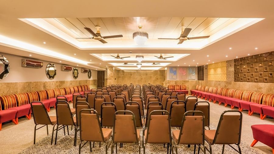 Rear view of the banquet hall, highlighting chairs meticulously arranged in rows, illuminated by warm lighting and accentuated by overhead ceiling lights