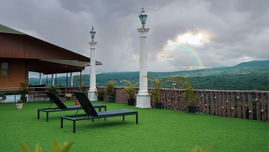 A view from the lawn on a cloudy day featuring a beautiful rainbow, beach chairs, and two light poles.