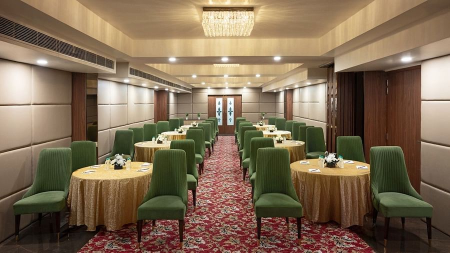 A well-lit conference room featuring round tables draped in golden tablecloths, surrounded by plush green chairs. A red patterned carpet runs through the centre of the space.  - Clarks Inn Express, Near Jammu Bari Brahmana Railway Station