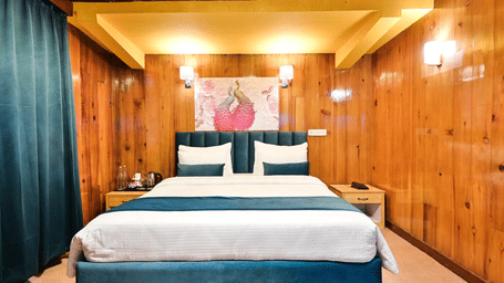 A cosy hotel room with a comfortable bed, wooden walls, and a painting above the headboard.
