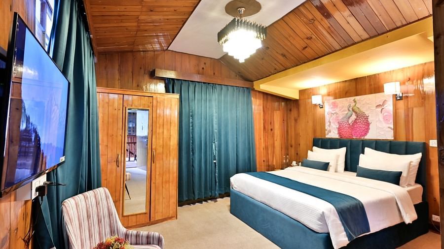 A cosy and well-furnished hotel room with a comfortable bed, a wardrobe, a television, and a seating area with a chair and a table.