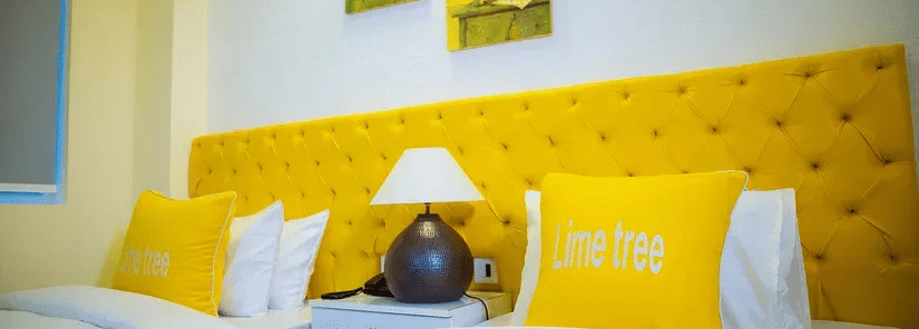 A room with twin beds, yellow cushioned headboard, and framed artwork on the white wall - Lime Tree Hotels & Banquet, Vrindavan