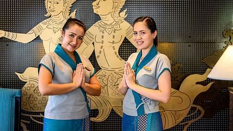 Two staff members, possibly of East Asian appearance, greet guests with traditional gestures in front of Thai artwork. - Maikhao Dream Villa Resort & Spa, Phuket