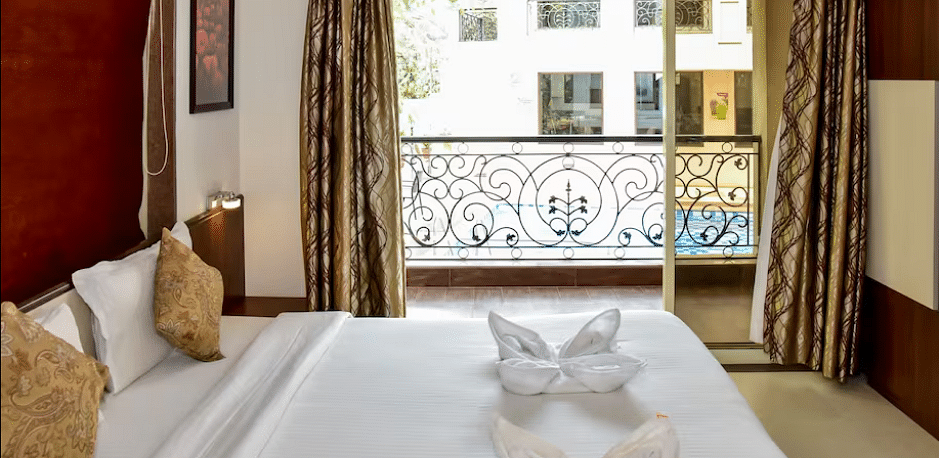 Cosy bedroom with golden cushions, towel swan decor, and a French balcony overlooking greenery at La Vida Studio Inn.