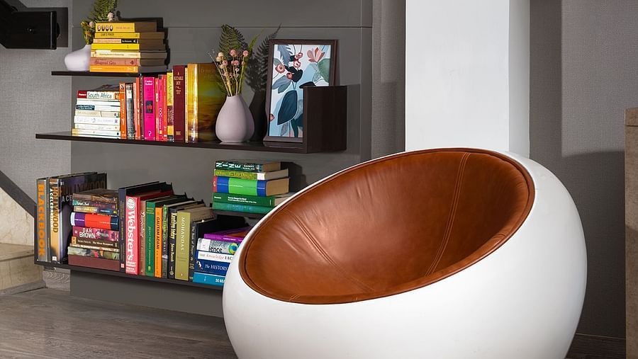 A modern living space at The Atara is highlighted by a tall, dark bookshelf brimming with various items, alongside a distinctive white spherical armchair