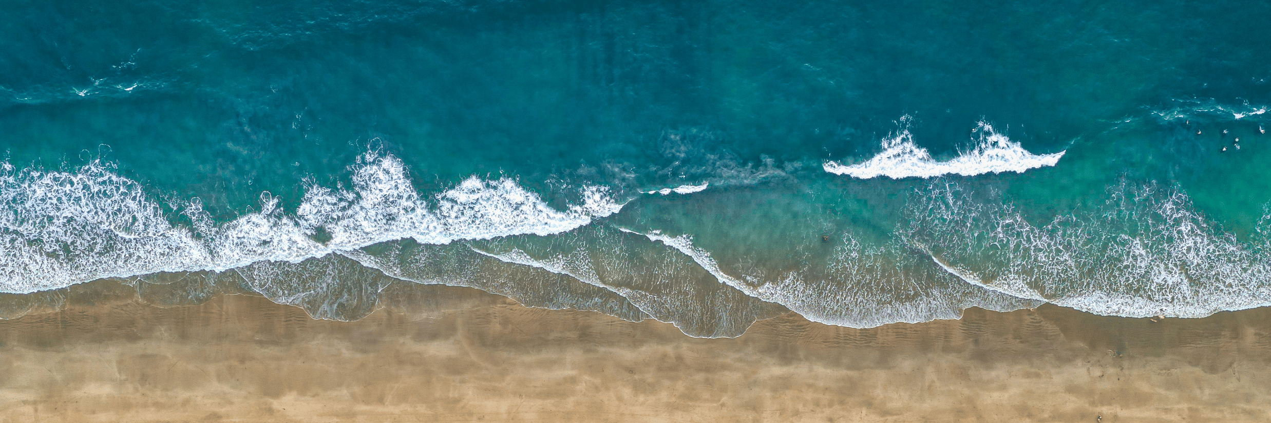 A top-down aerial view of Agonda Beach with the blue0green waves crashing on the shoreline.
