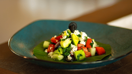 A small dish of fresh salad with diced vegetables and feta cheese at Stanley Revelation, on a dark plate.