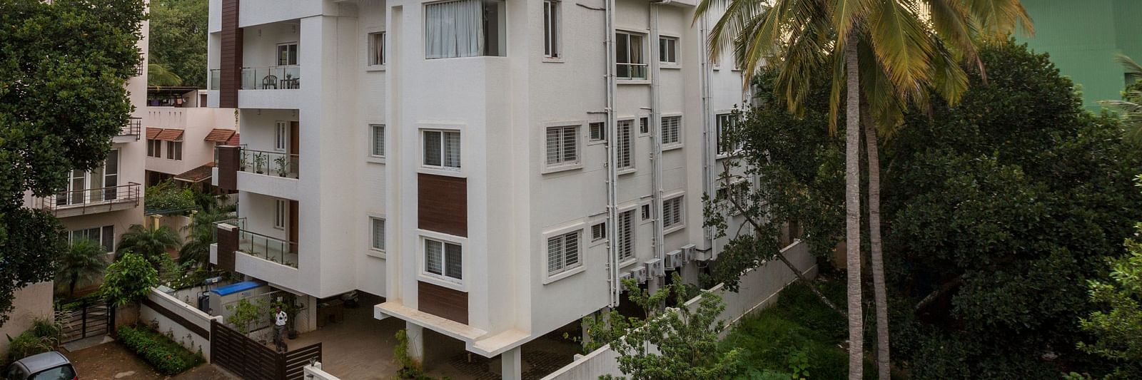 A light-coloured building exterior surrounded by green trees under a bright sky - Sanctum Suites BEL Road, Bangalore
