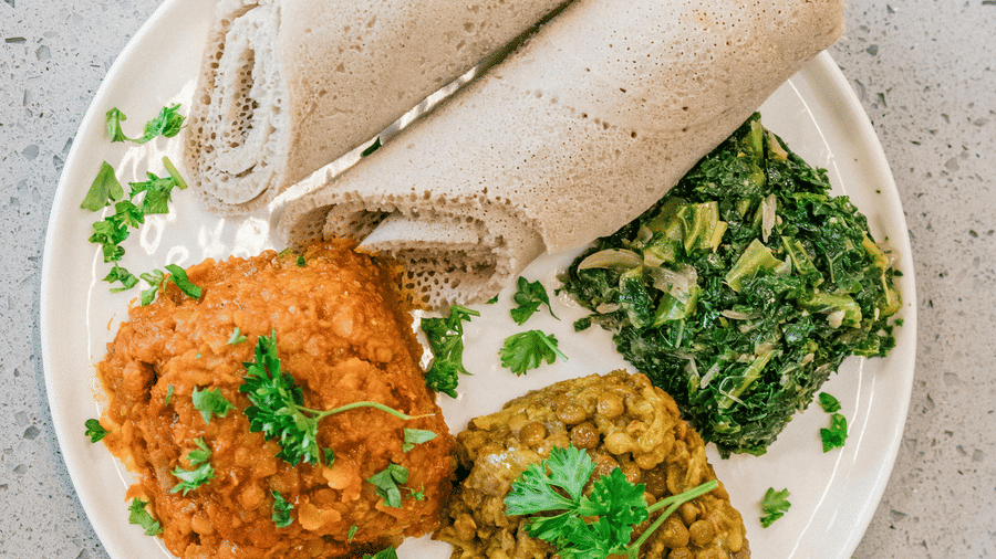 A plate containing injera and three veg side dishes on a patterned surface