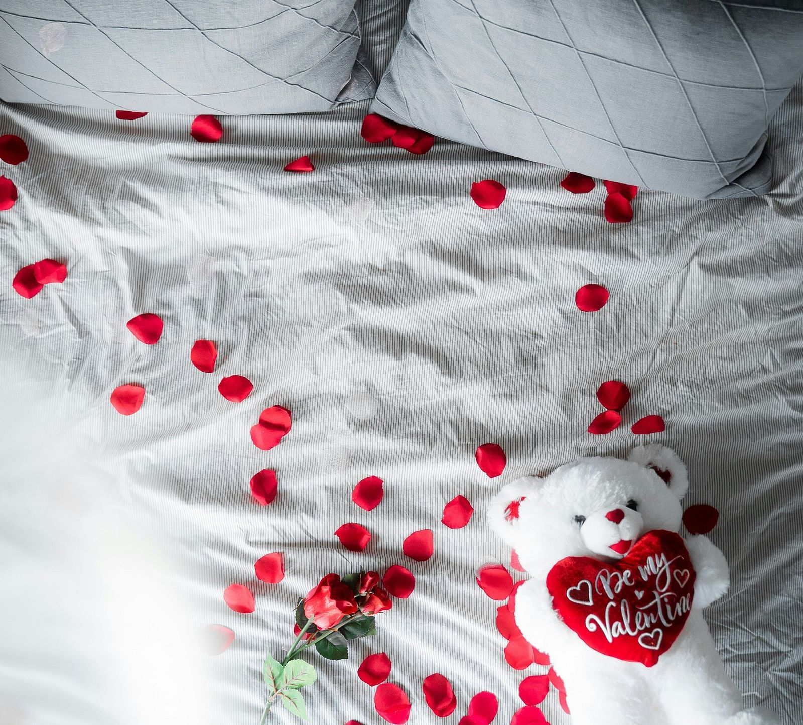 a bed with rose petals spread over and grey pillows on it 