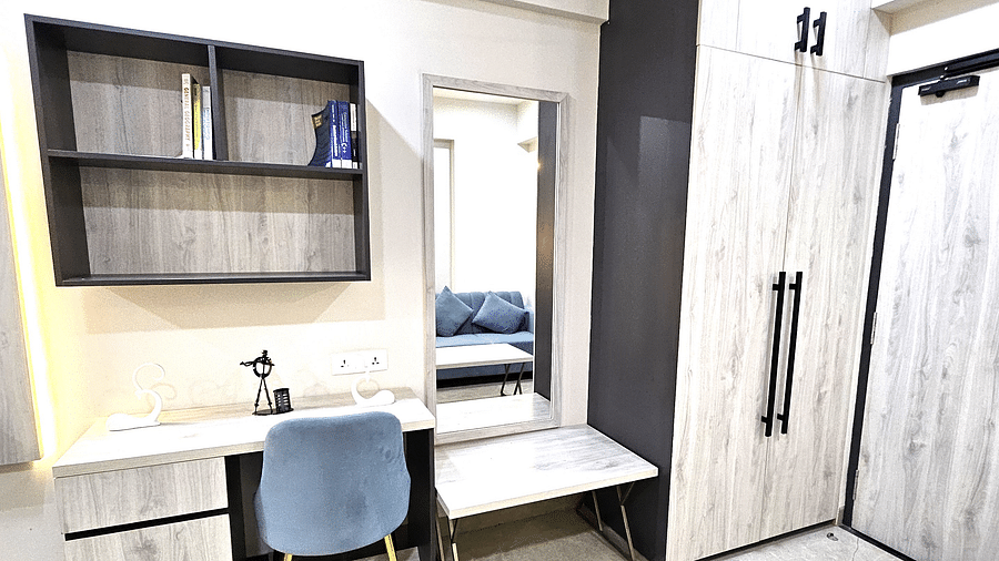 Modern workspace in a studio room featuring a sleek desk with storage, a comfortable upholstered chair, open shelves, a full-length mirror with a bench, and a spacious wardrobe for added convenience - Urban Suites by BluSalzz, Jaipur