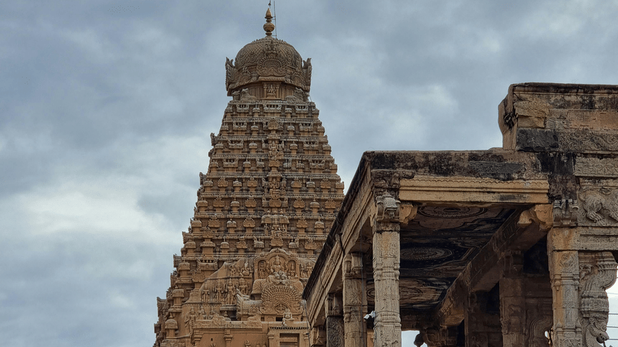Tourists and pilgrims gather at the ancient Brihadeeswarar Temple, admiring its grand Dravidian architecture under a cloudy sky.
