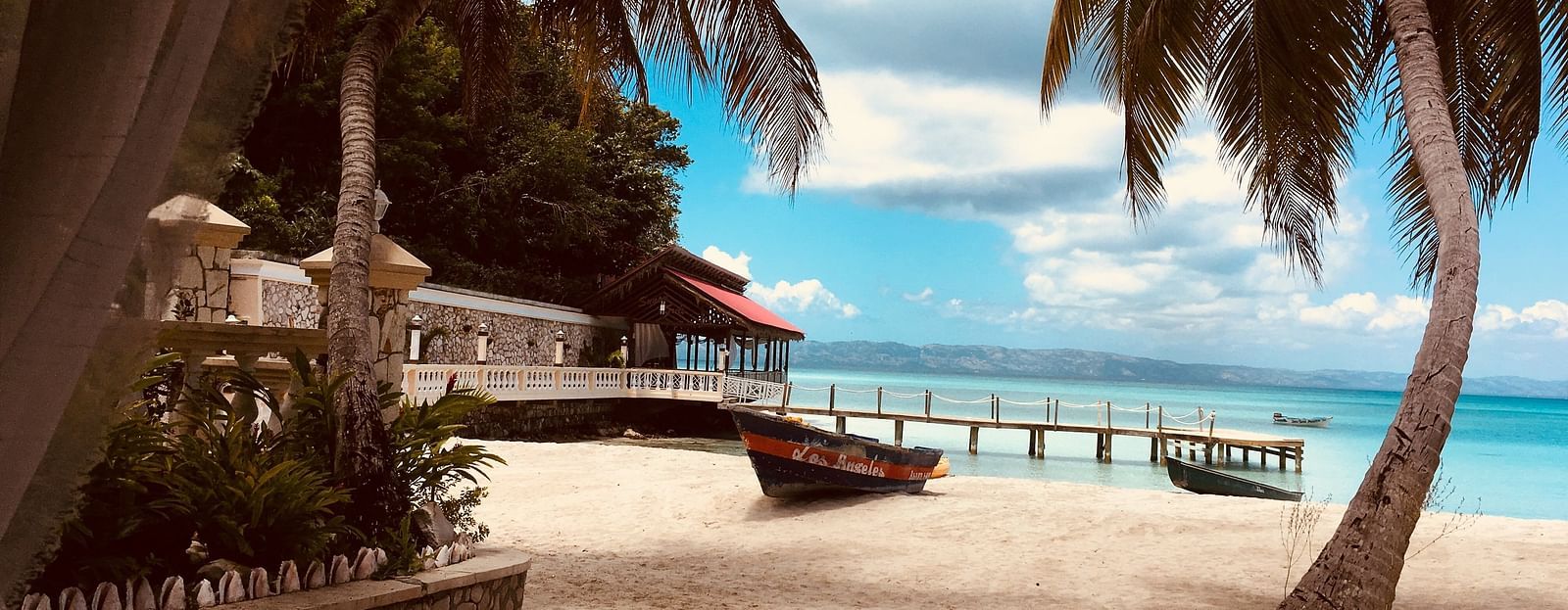 coconut trees and a boat on a beach with white clouds in the background
