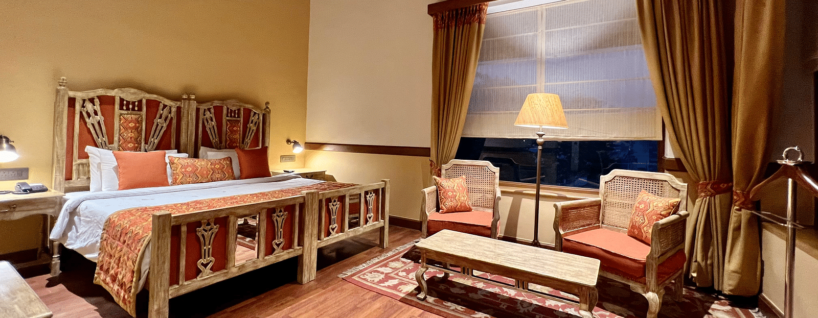 A cozy Superior Lake Facing Room at Fishermen's Lodge, Bhimtal, featuring a comfy bed, sofa, and table, perfect for relaxation.